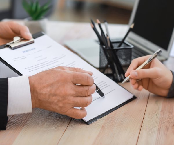 one person showing forms on a clipboard for another to sign